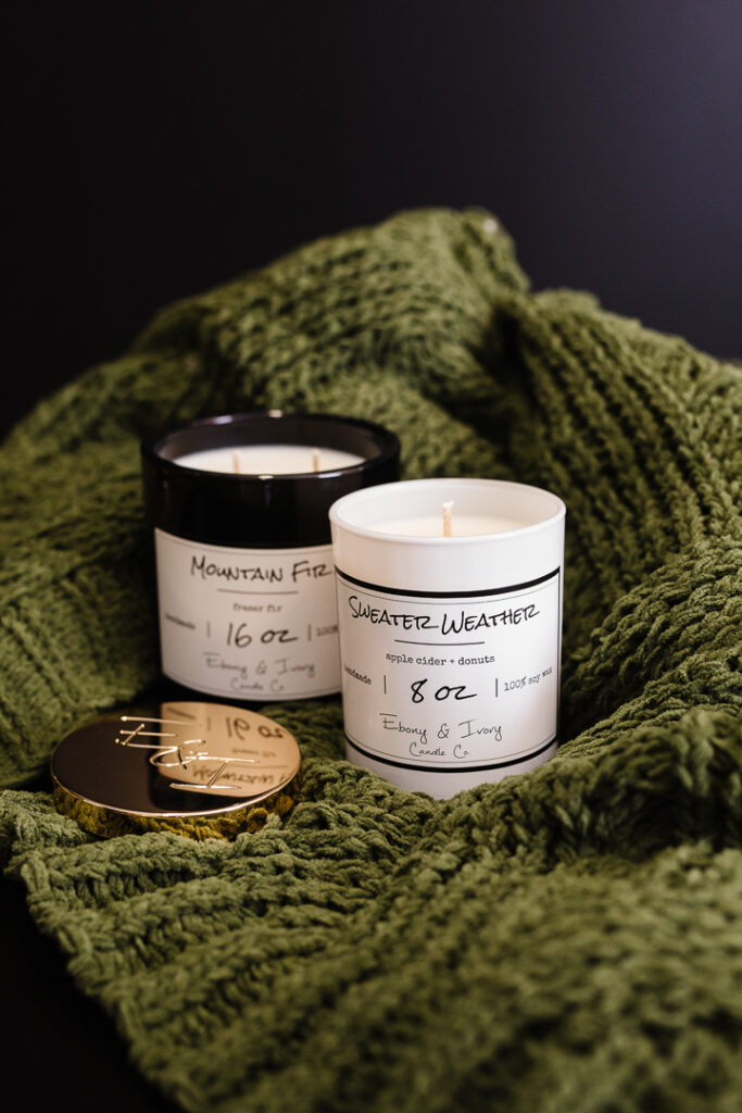 Two candles sitting on a sweater, made by Ebony & Ivory and Lethbridge product photos photographed by Kinsey Holt