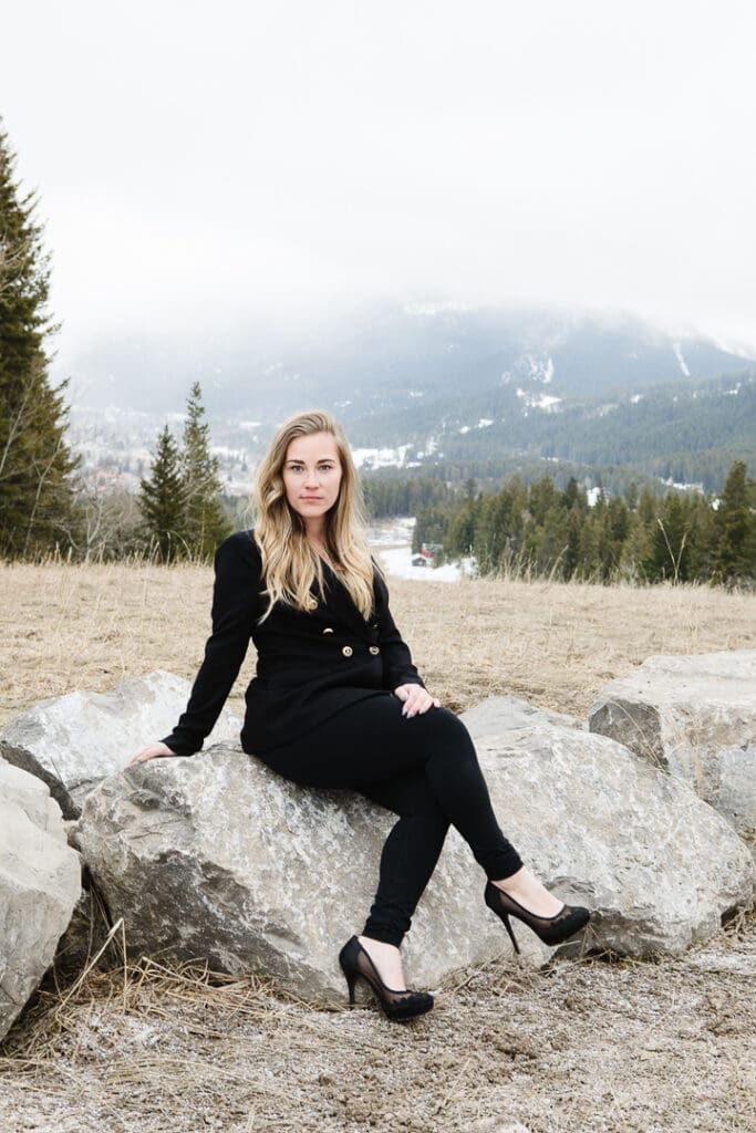 Woman in black suit sitting on boulder with mountain view behind her. Realtor brand photos.