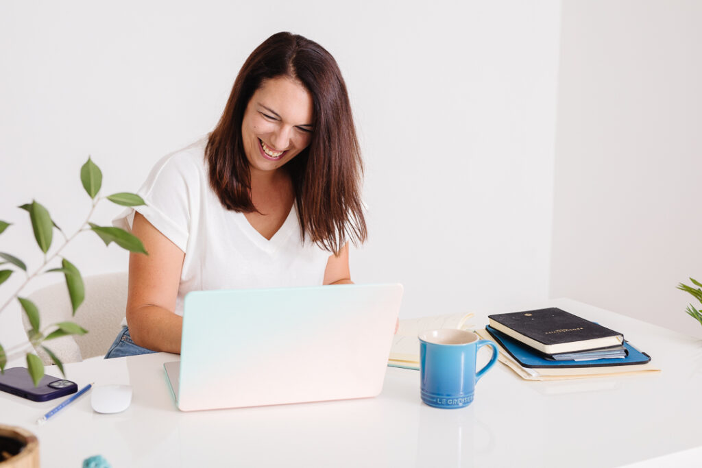 Virtual assistant brand photos showing woman smiling at laptop with blue coffee mug beside her.