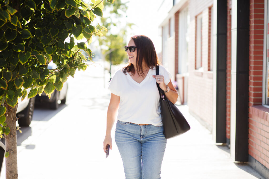 Woman walking down sidewalk, purse on shoulder.